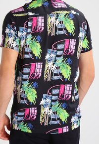 Camisa de manga corta en tejido negro con un vibrante estampado tropical de palmeras y ventanas en colores rosa, verde y azul.