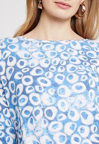 Blauses Oberteil mit gemusterten ovalen Formen in Weiß und Hellblau, aus einem weichen Stoff mit glatter Textur. Rundhalsausschnitt.