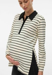Polo shirt per maternità con colletto e bottoniera nera, tessuto crema con strisce orizzontali nere, spacco laterale per un comfort aggiuntivo.
