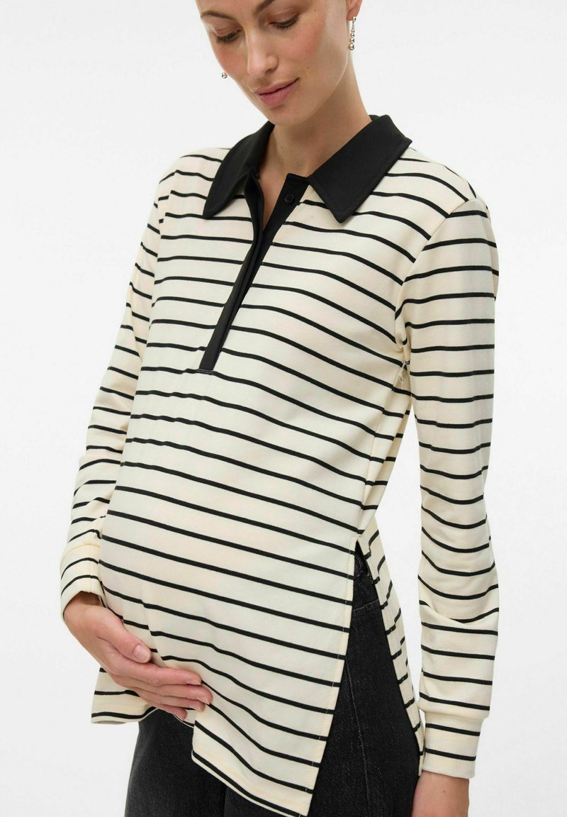 Polo shirt per maternità con colletto e bottoniera nera, tessuto crema con strisce orizzontali nere, spacco laterale per un comfort aggiuntivo.