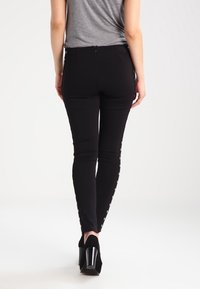 Czarne dopasowane spodnie o gładkiej teksturze, z zapięciami na zatrzaski po obu stronach oraz wysokim stanem.
