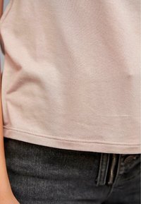 T-shirt en coton rose clair avec une texture lisse, manches courtes et ourlet droit, accompagné d'un jean en denim gris foncé avec une fermeture éclair.