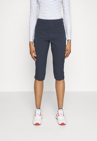 Marina cropped sportbyxor med stretchmidja och sidostripes. I kombination med vita sneakers med röda detaljer. Slät textur.