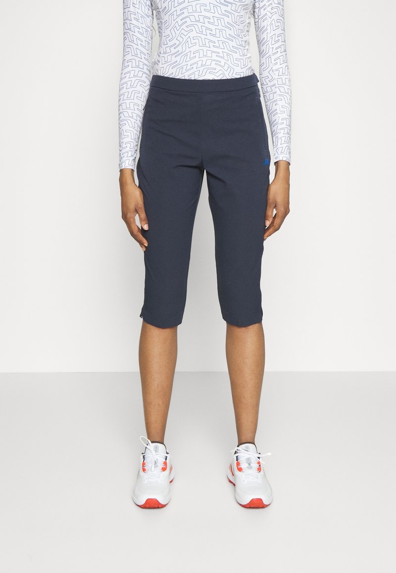 Marina cropped sportbyxor med stretchmidja och sidostripes. I kombination med vita sneakers med röda detaljer. Slät textur.