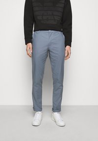 Světle modré chinos kalhoty se slim fit střihem, nastavitelným pasem, bočními kapsami a ohrnutými manžetami, doplněné černou mikinou a bílými teniskami.