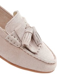 Mocasin de ante rosa claro con un acabado texturizado, que presenta un fleco decorativo y detalle de lazo en la parte superior y un ribete cosido.