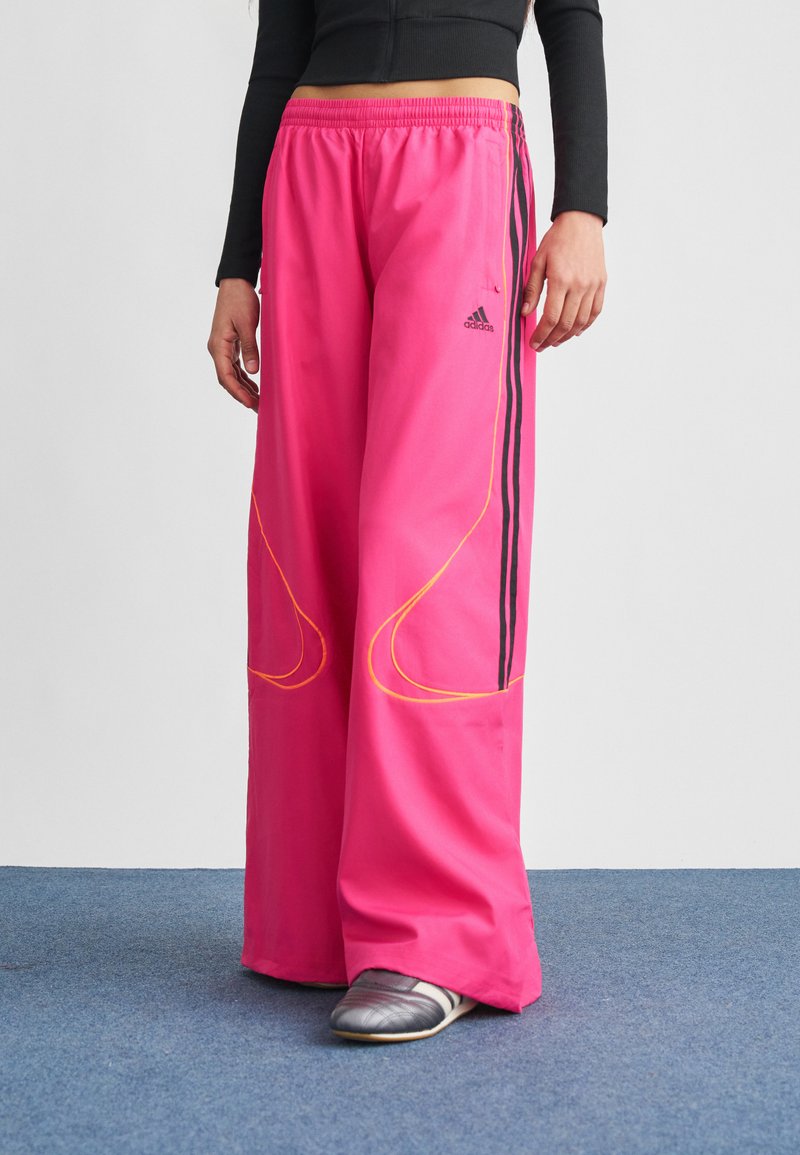 Rózsaszín, bőszárú nadrág könnyű anyagból, fekete oldalsávokkal és sárga varrással, kényelmes gumis derékrésszel.