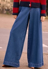 Vidje-bukser i mörkblå denim med hög midja, ljusa sömmar och avslappnad passform. Accentuerade med en enkel fåll och subtil textur.