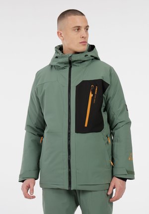 Chaqueta aislante verde con un bolsillo en el pecho negro, cremallera naranja, capucha ajustable y bolsillos laterales con cremallera. Textura suave, diseño moderno.