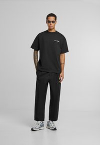 Sort bomulds t-shirt med korte ærmer og et lille hvidt logo, parret med sorte bukser og metalliske sneakers med accenter.