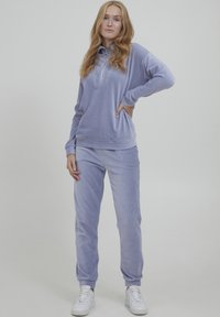 Helles lila Velours-Trainingsanzug mit einem Kragen-Pullover mit einem Viertel-Reißverschluss und passenden tapered Hosen mit elastischen Bündchen.