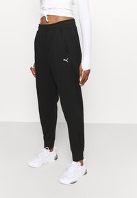 Zwarte joggingsbroek van zacht materiaal, met een elastische tailleband, zijzakken en een klein wit logo op de linkerdij.