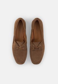 Bruine suède schoenen hebben een klassiek bootdesign, veters en accenthardware. De binnenkant is van soepel leer met stiksels rondom de randen.