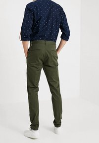 Olivgrüne Chinos mit Slim-Fit und normalen Taschen, kombiniert mit einem navyblauen Hemd mit Knöpfen, das weiße Punkte aufweist.