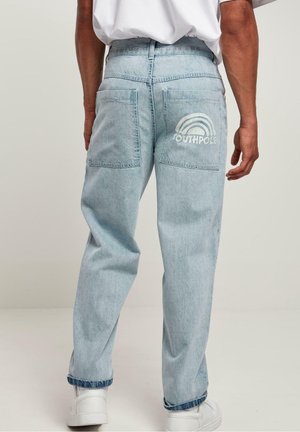 Mand iført lyseblå jeans med store baglommer og en hvid "SOUTHPOLE"-logo under et regnbuedesign på højre lomme.