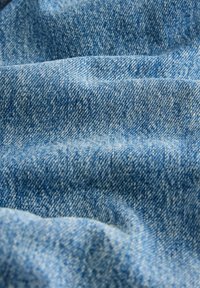Gros plan d'un tissu en denim bleu clair montrant une texture tissée détaillée et des plis doux.