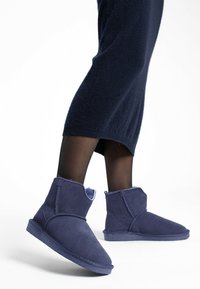 Botines de ante azul oscuro con forro interior suave y texturizado, que presentan un diseño simple y minimalista con suela plana.