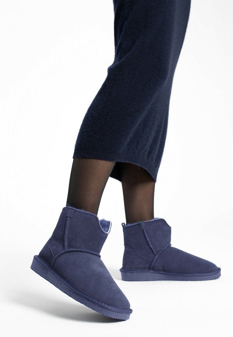 Botines de ante azul oscuro con forro interior suave y texturizado, que presentan un diseño simple y minimalista con suela plana.