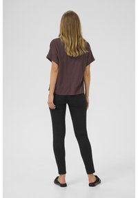 Blouse à manches courtes, à coupe ample, en tissu violet foncé, associée à un jean noir ajusté. Des sandales décontractées complètent le look.