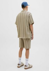 Chemise à manches courtes à carreaux brun clair et short assorti, fabriqués en tissu texturé. Porté avec une casquette bleue et des baskets beiges, chaussettes blanches.