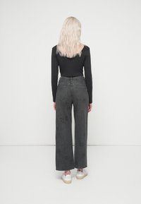 Μαύρη μπλούζα μακρυμάνικη συνδυασμένη με ψηλόμεσα, φαρδιά γκρίζα τζιν με υφασμάτινα σχέδια και δυο πίσω τσέπες. Λευκά sneakers ολοκληρώνουν το σύνολο.