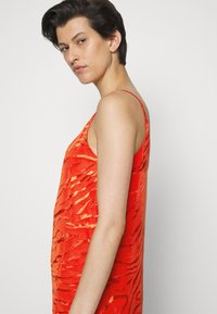 Vestido vermelho sem mangas com um corte ligeiramente solto, apresentando um padrão zebra texturizado e um tecido suave. O design inclui alças finas.