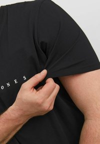 Zwarte T-shirt van katoen, met een ronde hals en korte mouwen. Opvallend wit tekstontwerp over de borst; gladde textuur.