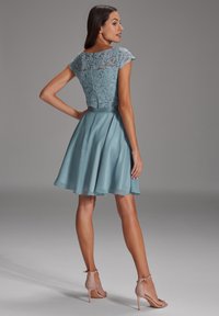 Une robe bleu ciel avec un corsage en dentelle, une jupe satinée évasée et de courtes manches à capuchon. Assortie à des sandales à talons hauts beiges.