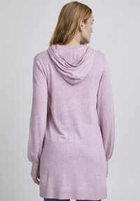 Hoodie rose clair, à manches longues, en tissu doux et texturé, présente une coupe décontractée et une capuche profonde dans le dos, avec des bords côtelés aux poignets et à l'ourlet.