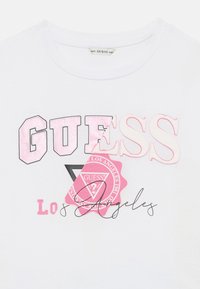 T-shirt bianca in cotone con loghi stampati multicolori in nero e rosa, con scollatura tonda e maniche corte.