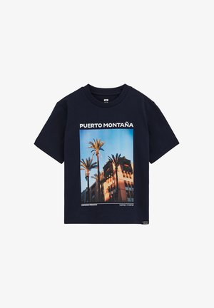 Tumesinine puuvillane t-särk, mille keskel on palmipuude ja hoone graafika ning üleval valge tekst "PUERTO MONTAÑA". Lühikesed varrukad.