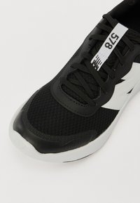 Czarne sportowe buty z siateczkowej cholewki z czarną skórzaną nakładką, białymi akcentami i wyściełaną białą podeszwą.