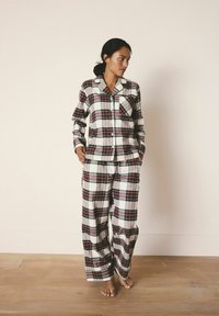 Plaid pajama set in white, red, and green with button-up shirt and loose-fitting pants. Made from soft fabric with a chest pocket.