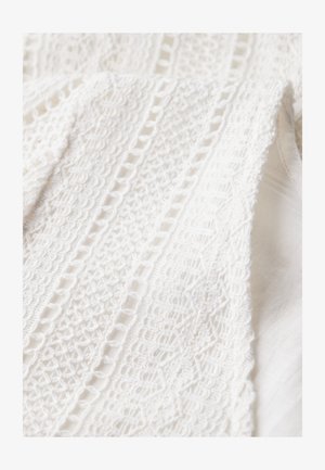 Witte kanten stof met ingewikkelde patronen, waaronder geometrische vormen en getextureerde gebieden, gelaagd op een gladde witte achtergrond.