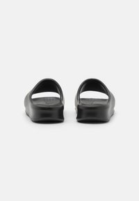 Chanclas de goma negra con parte trasera abierta y una base texturizada. Diseño minimalista con bordes redondeados y superficies lisas.