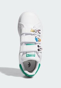 Sneakers sintetici bianchi con tre cinturini in velcro che presentano accenti dei personaggi dei cartoni animati di Topolino, Paperino e Pippo. Dettaglio verde sul tallone.
