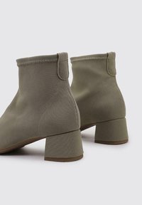 Bottines en toile vert olive avec une finition texturée, présentant un bout arrondi et un petit talon carré. Les surpiqûres ajoutent de la structure.