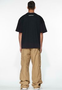 Svart oversized t-skjorte med korte ermer, har et logo på baksiden. Kombinert med khaki cargo-bukser med flere lommer.