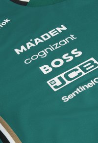 Teal sports jersey med rund halsudskæring, forsynet med hvid branding og logoer fra MAADEN, Cognizant, BOSS, JCB og Sentinel.