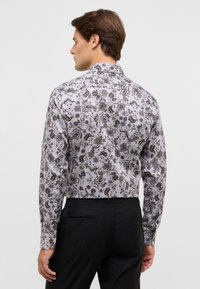 Langsleeve shirt met een bloemenpatroon in bruintinten op een lichte achtergrond. Kenmerkt zich door een hoge kraag en een aansluitend ontwerp, gecombineerd met zwarte broek.