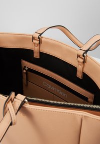 Calvin Klein tote bag van zacht perzik materiaal. Voorzien van zwarte voering, binnenzak met rits en dubbele hengsels aan de bovenkant. Ritsluiting aan de bovenkant.