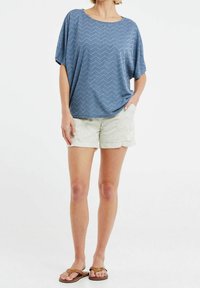 Top de manga corta con estampado azul y corte holgado, combinado con pantalones cortos beige claro y chancletas marrones. Atuendo casual de verano.