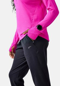 Maglia fucsia a maniche lunghe con polsini testurizzati abbinata a pantaloni sportivi neri con tasca laterale con zip e logo riflettente.