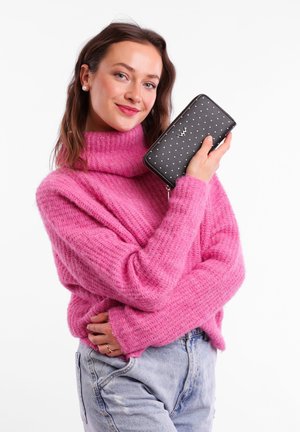 Black zipped wallet with white polka dots, featuring a silver logo accent. Pairing with a pink chunky knit sweater and light-wash jeans.