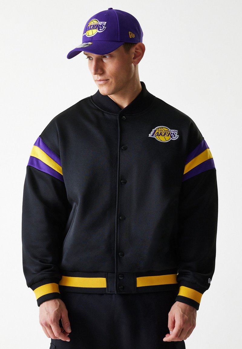 Black bomber jacket with purple and yellow stripes on sleeves, featuring a Los Angeles Lakers logo. Ribbed cuffs and waistband.