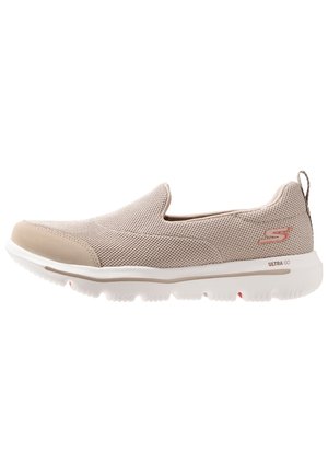 Hellbeiger Slip-On Sneaker mit atmungsaktivem Mesh-Obermaterial, weißer flexibler Sohle und Markenlogo an Ferse und Seite.