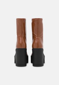 Brown patent leather ankle boots with a sleek design, high black block heels, and visible stitching along the seams.