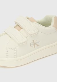 Športni copat Calvin Klein v kremni barvi z dvema ježkoma in bež notranjo oblogo, prikazan na belem ozadju.