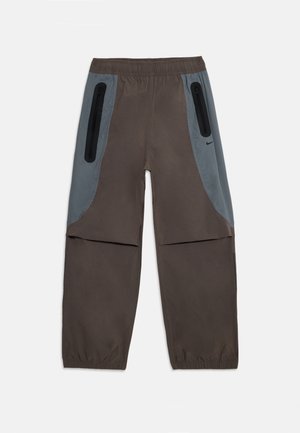 Brune bukser med grå sidepaneler, elastisk talje og to glidelommer. Stoffet virker glatt og lett.