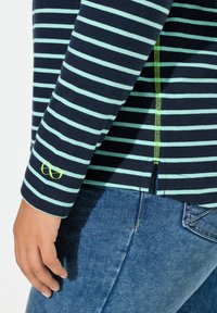 Námořnický pruhovaný top s dlouhým rukávem se světle modrými pruhy, zdobený zeleným logem na manžetě a středním zadním švem s kontrastním prošitím.
